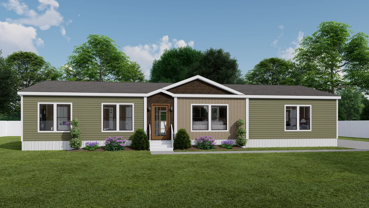 A single-story manufactured home with green and beige siding, multiple windows, a central front door, shrubs, and a manicured lawn, set against a backdrop of trees and blue sky.