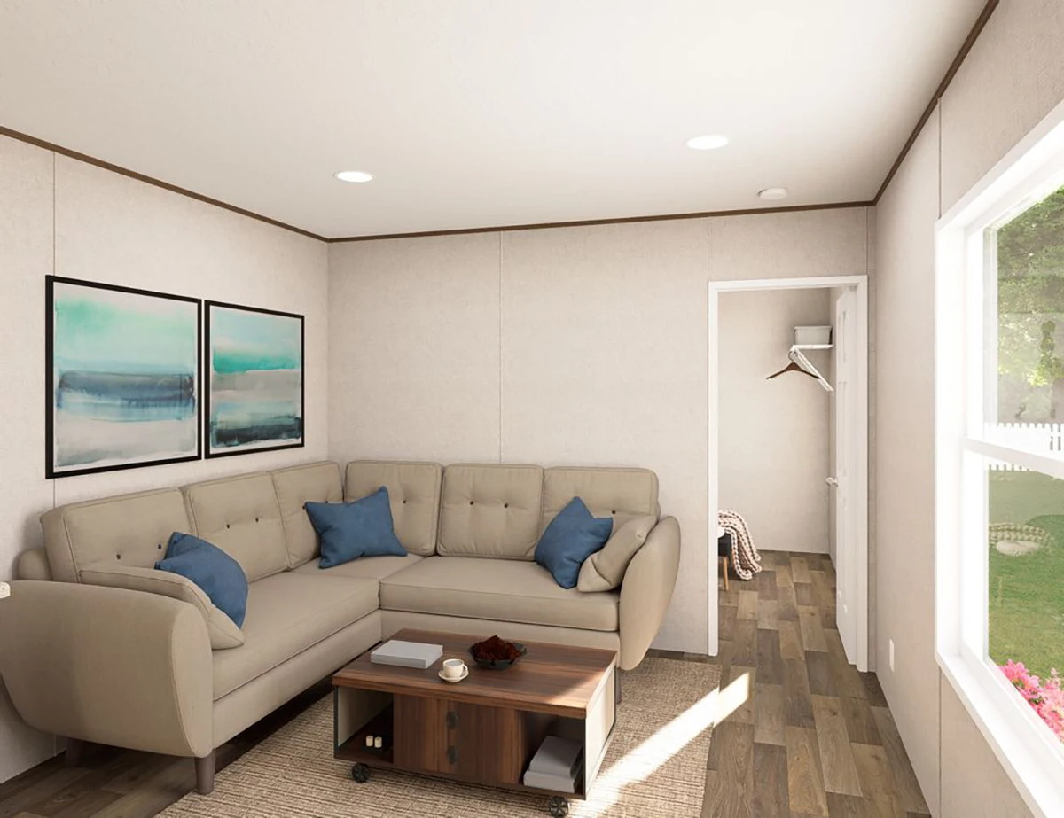 A modern living room with a beige sectional sofa, blue pillows, two abstract artworks, a wooden coffee table, and an open door leading to a small entryway with a window view.
