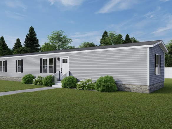 A single-story gray manufactured home with white trim, front steps, and surrounded by green grass and shrubs under a blue sky.