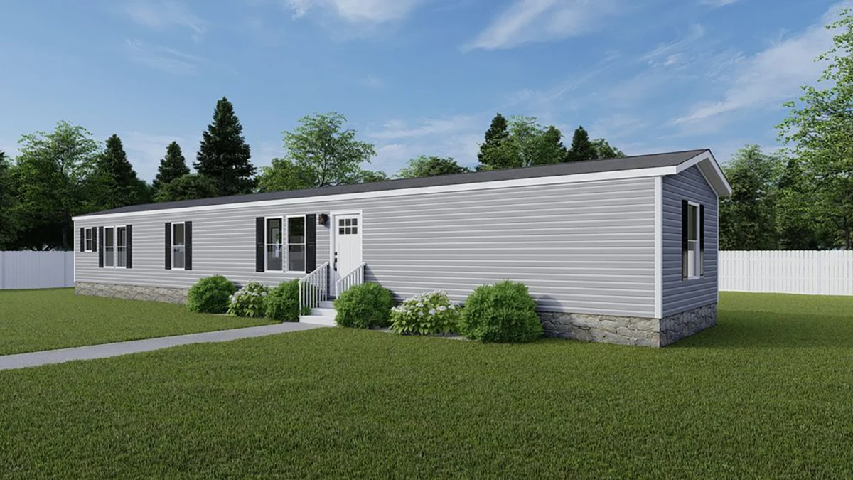 A single-story gray manufactured home with white trim, front steps, and surrounded by green grass and shrubs under a blue sky.