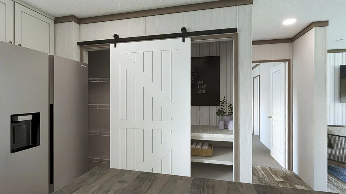 A modern kitchen with a sliding barn door revealing pantry shelves, adjacent to a refrigerator and light wood cabinetry.