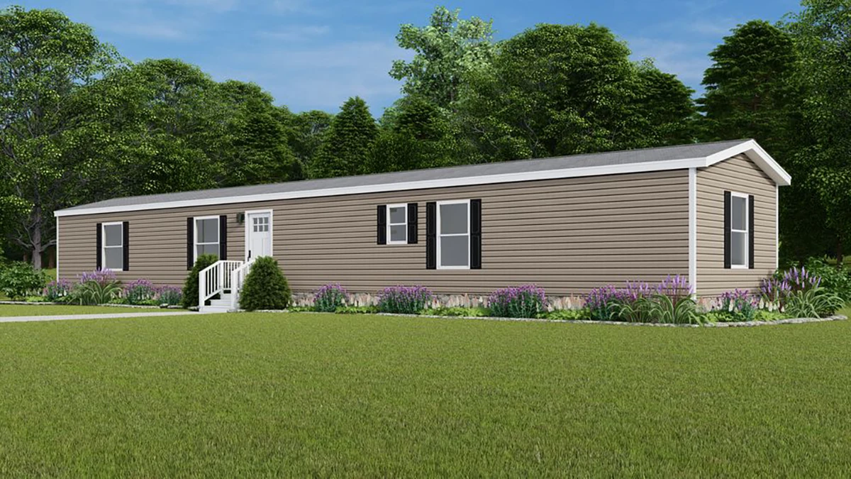 A single-story, beige manufactured home with white trim and black shutters, surrounded by grass, shrubs, and trees under a blue sky.