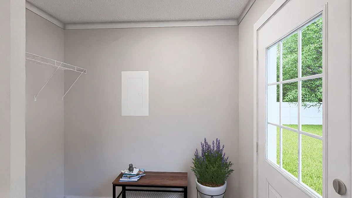 A small entryway with a white door, a wooden bench holding books, a potted plant, and a wire shelf on a plain light gray wall. Grass and trees are visible outside.