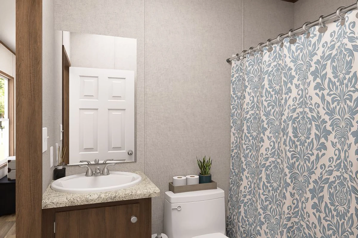 fc5f0b09-72f4-4155-9531-23159ce3fff4 A small bathroom with a sink, mirror, toilet, two toilet paper rolls, a potted plant, and a shower with a blue and white patterned curtain.
