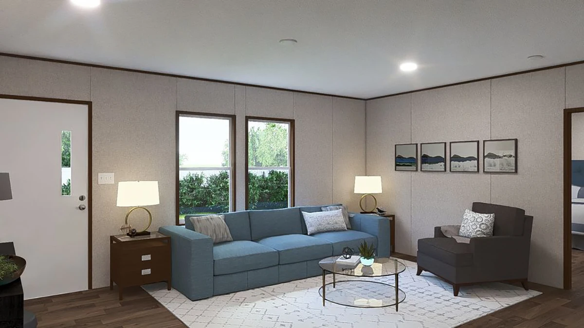 A modern living room with a blue sofa, gray armchair, round glass coffee table, two table lamps, wall art, and large windows letting in natural light.