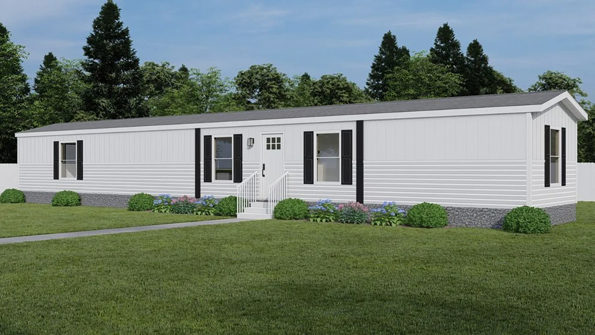 A white single-wide manufactured home with black shutters, a small stoop with steps, surrounded by a lawn, bushes, and trees in the background.