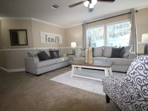 A living room with two gray sofas, a patterned armchair, a wooden coffee table, and large windows with gray curtains letting in natural light.