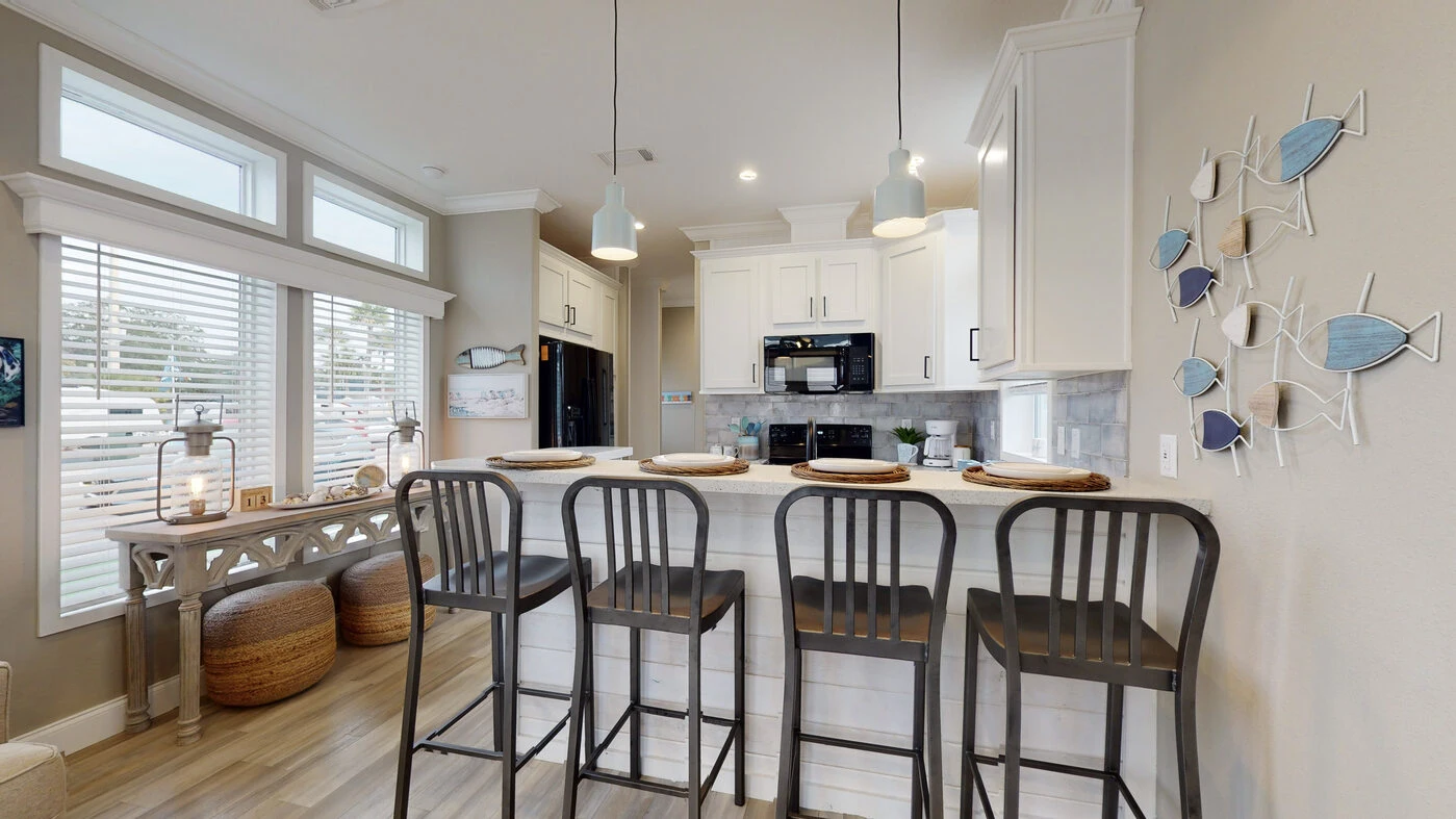 Modern kitchen with white cabinets, black appliances, a breakfast bar with four metal stools, and decorative fish wall art. Large windows provide natural light.