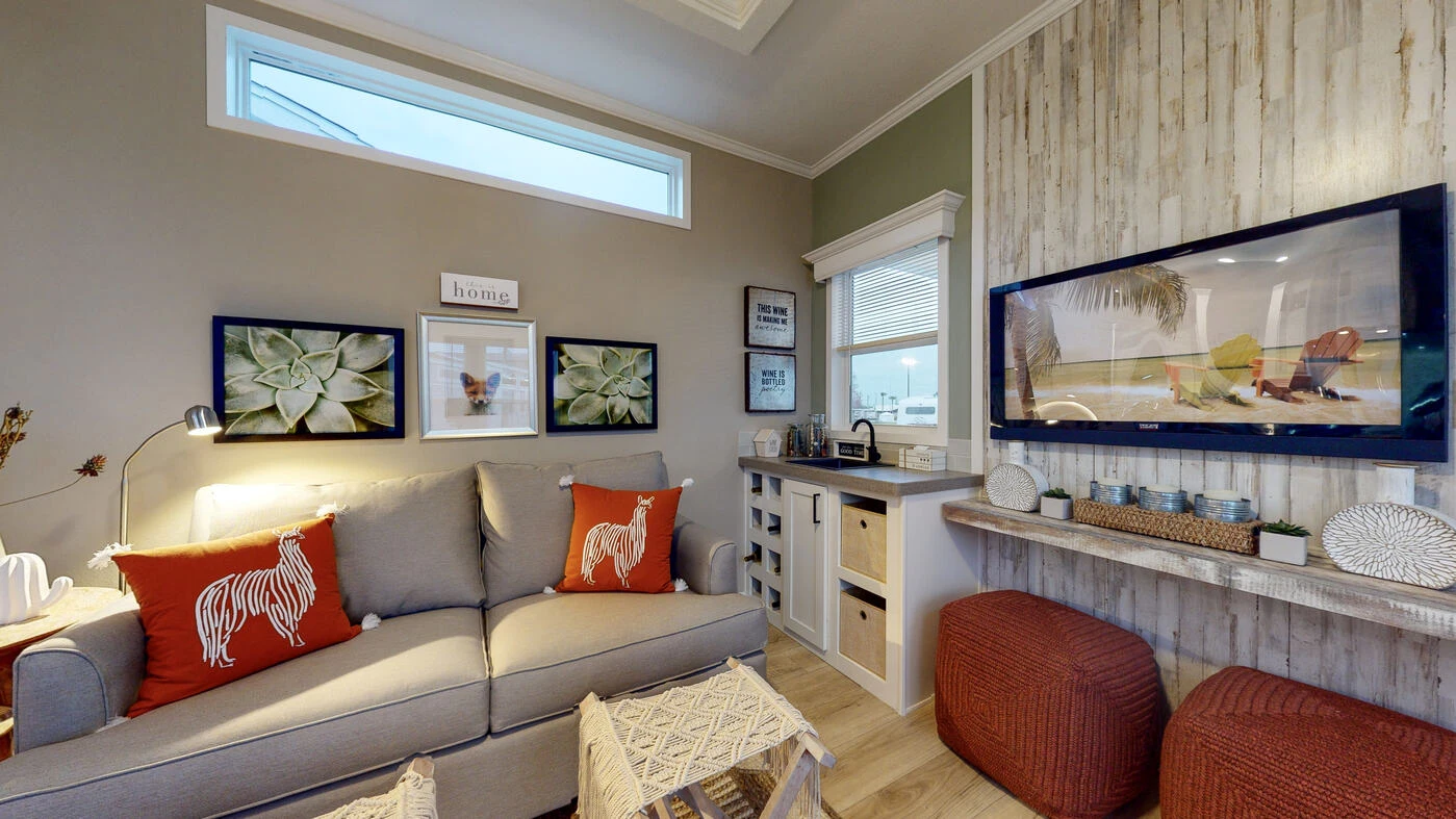 Cozy living room with a gray sofa, red pillows, wall art, a flat-screen TV, two red ottomans, and a shelf with decorative items on a wood accent wall.