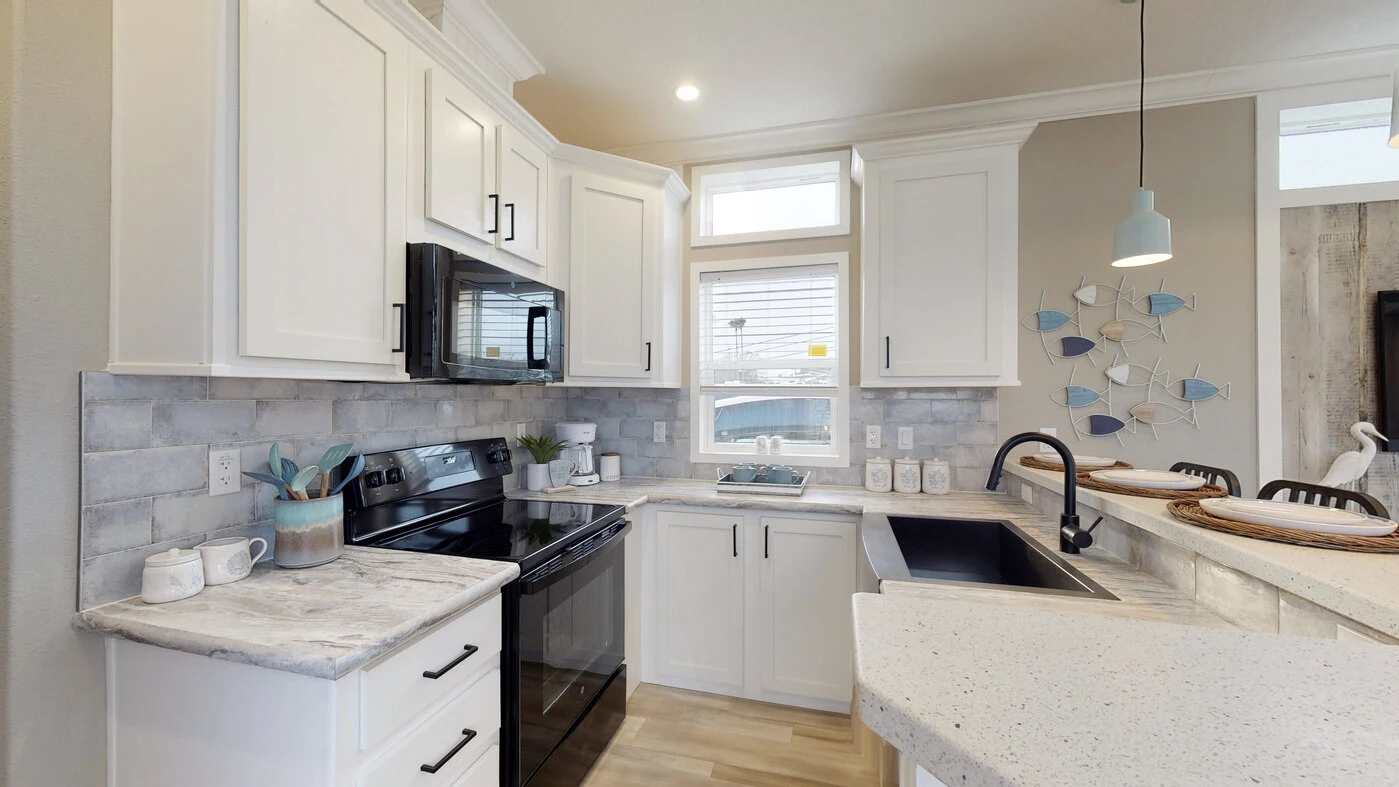 Modern kitchen with white cabinets, black appliances, marble countertops, and a decorative wall with fish accents. Daylight streams in through two windows above the sink.