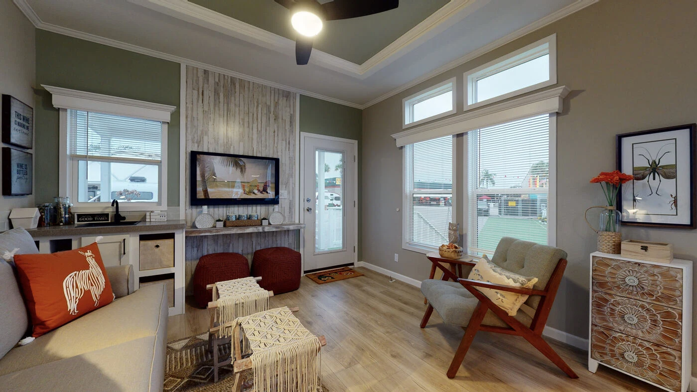 A cozy living room with wood floors, modern furniture, large windows with blinds, wall art, a TV, and decor including throws and plants.