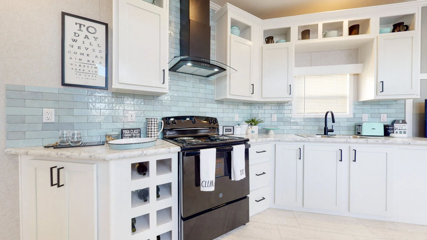 Modern kitchen with white cabinets, light blue subway tile backsplash, black stove, glass-front cabinets, and countertop appliances. Window above sink lets in natural light.