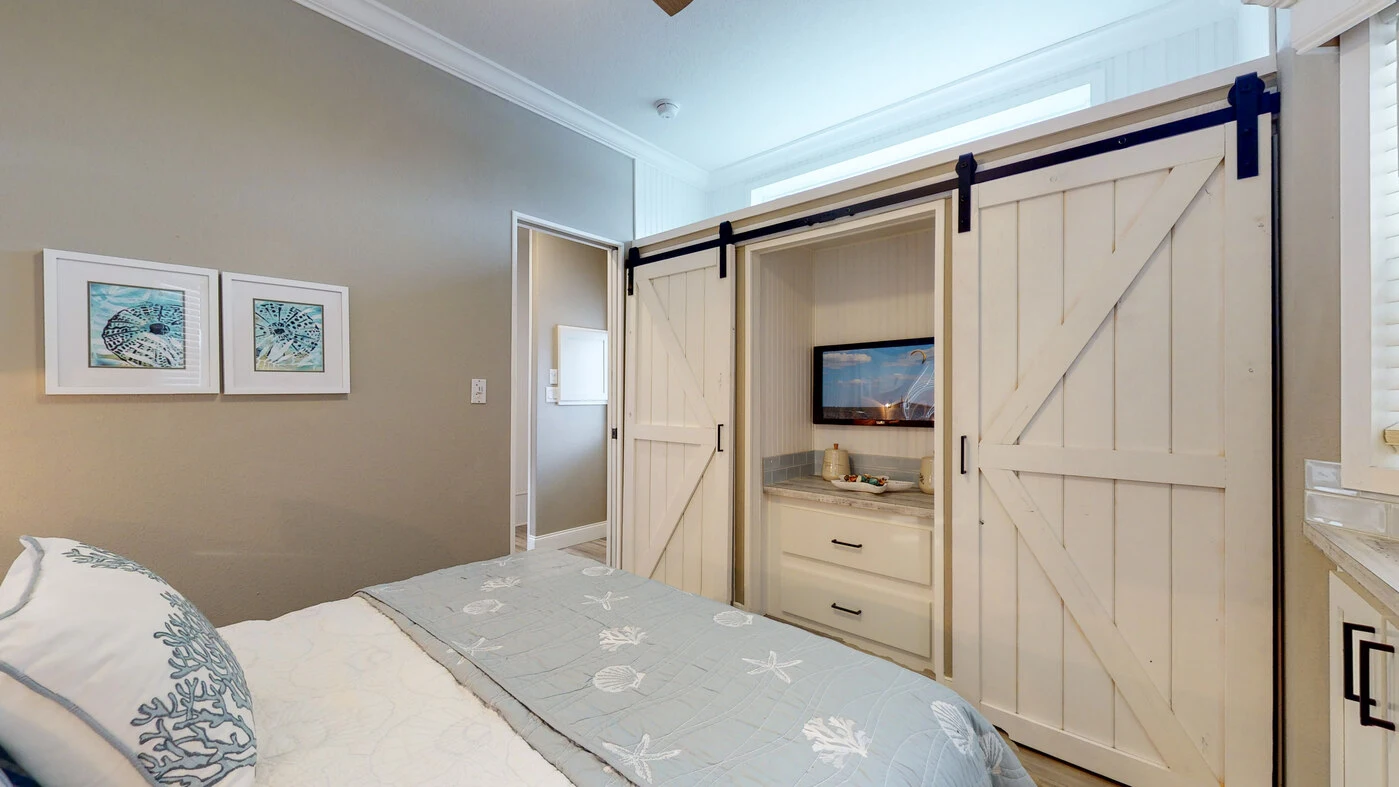 Bedroom with a bed, two framed artworks on the wall, and a TV placed in a cabinet with sliding barn doors.