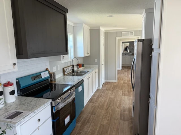 Galley-style kitchen with white cabinets, marble countertops, stainless steel appliances, and wood-look flooring, leading to a hallway with multiple doorways.