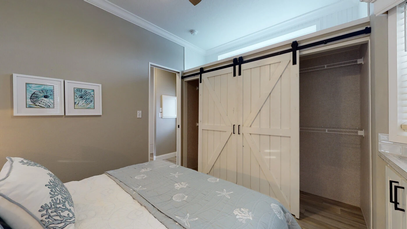 Bedroom with a bed in the foreground, two framed prints on the wall, and an open closet with white sliding barn doors.