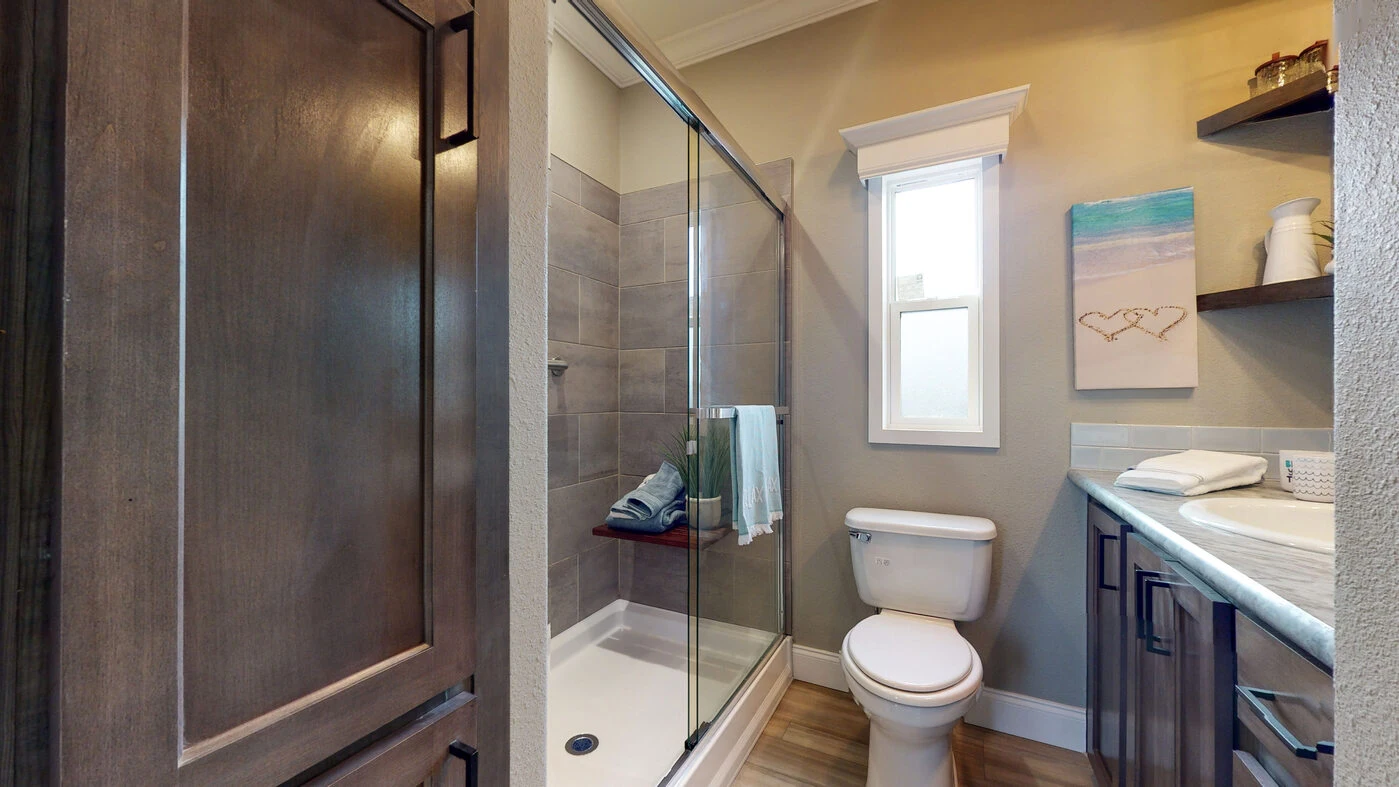 Modern bathroom with a glass-enclosed shower, toilet, countertop with sink, open shelves, and a window letting in natural light.