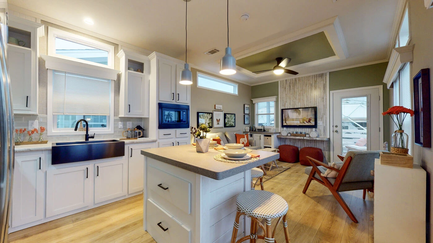 Modern open-concept kitchen and living area with white cabinets, center island, dining setup, and cozy seating area near a wall-mounted TV and fireplace.