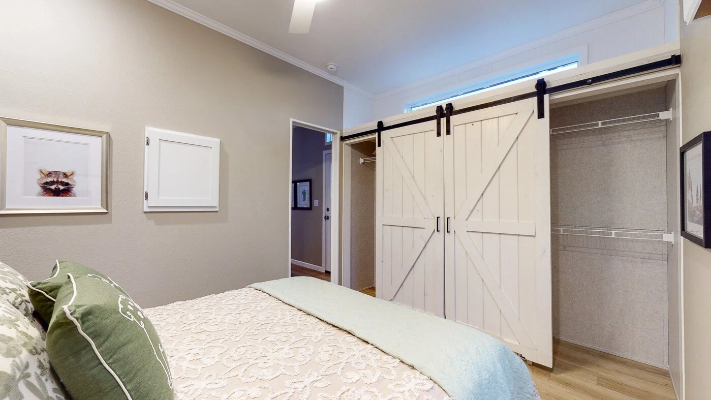Bedroom with a bed, patterned bedding, framed artwork on the wall, and an open closet with white sliding barn doors.
