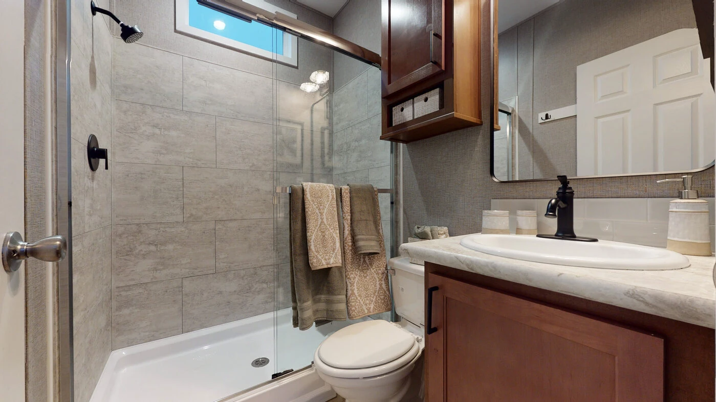 Modern bathroom with a glass-enclosed shower, beige tiles, brown cabinetry, a white toilet, and a countertop with a black faucet and soap dispensers.