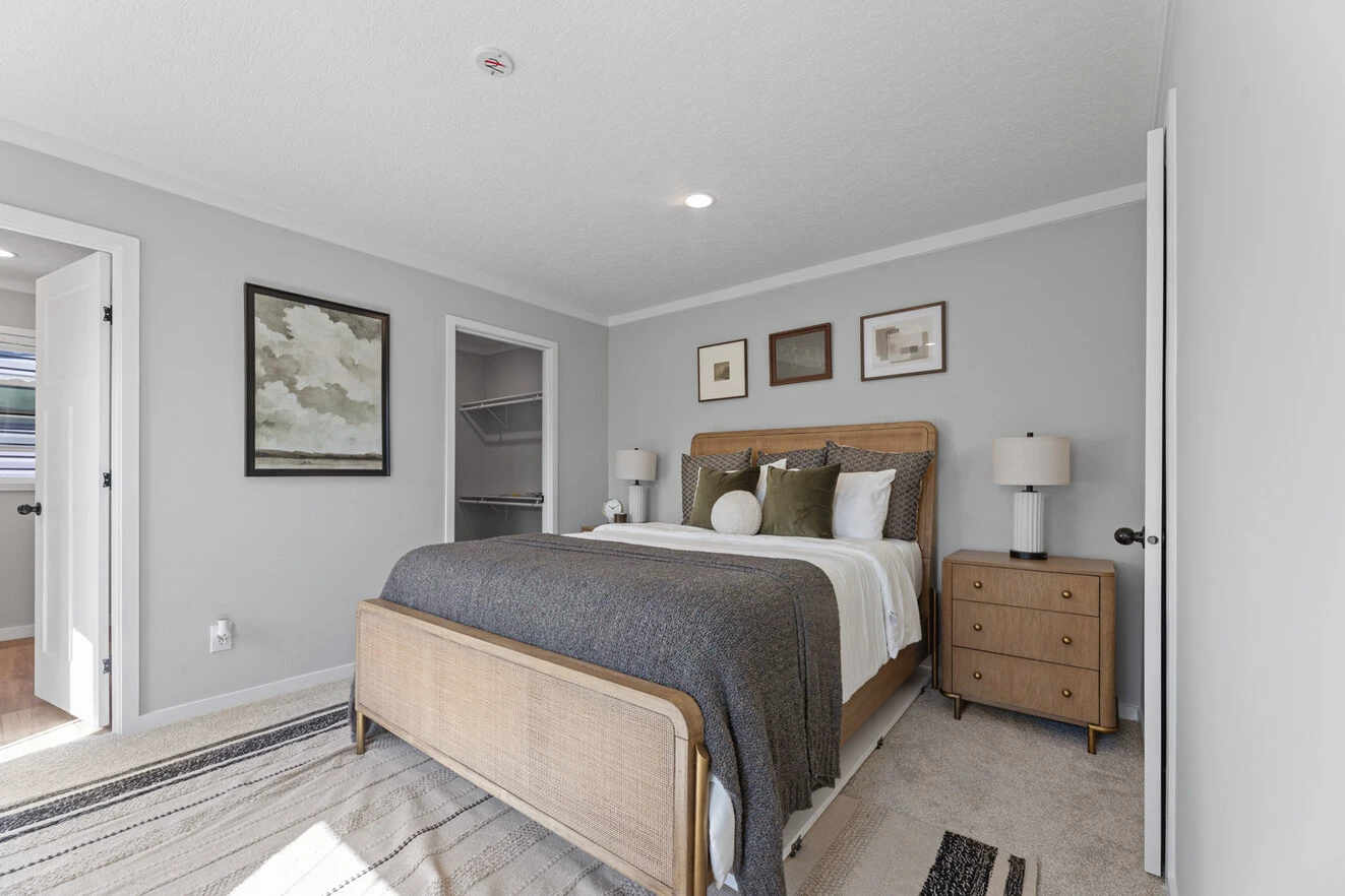 25_c_290_helix_1763n_bed_006_web_1742588921454_1323_12 A modern bedroom with a wooden bed, gray bedding, two nightstands with lamps, framed art on gray walls, and an open door to a walk-in closet.