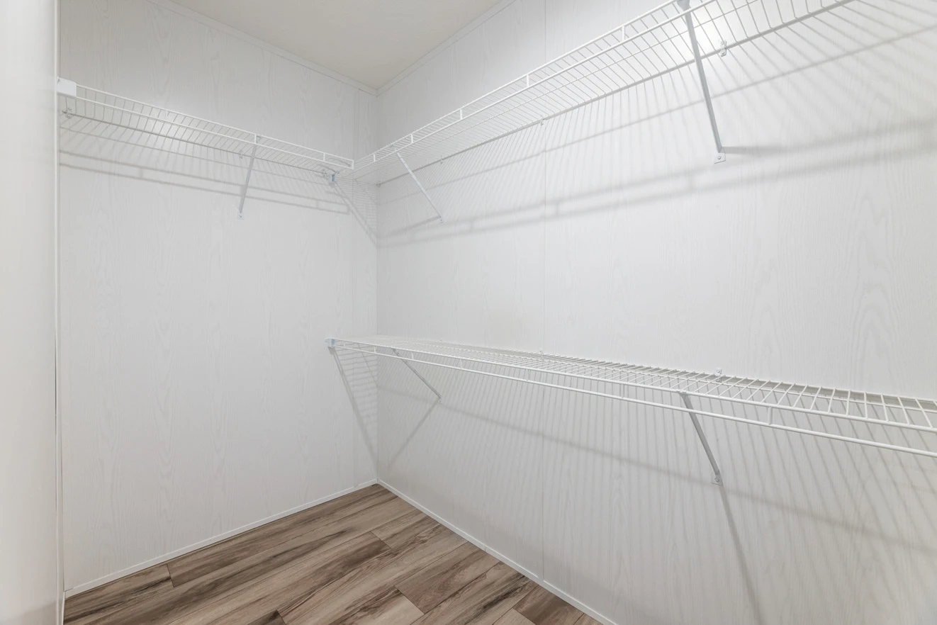 Empty walk-in closet with white wire shelves on three walls and light wood-patterned flooring.