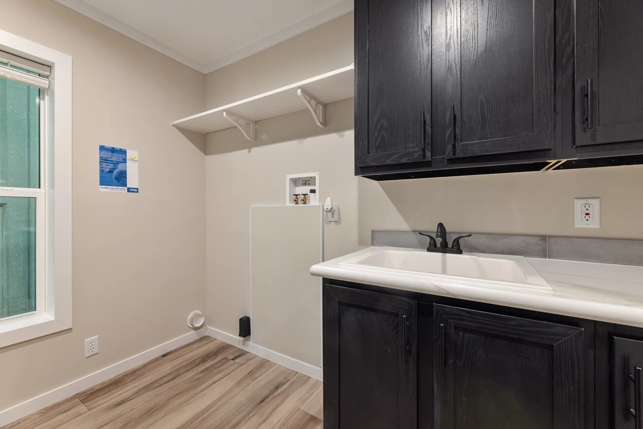 Laundry area with an empty washer/dryer hookup, upper shelf, dark cabinets, a white utility sink, and wood-patterned flooring.