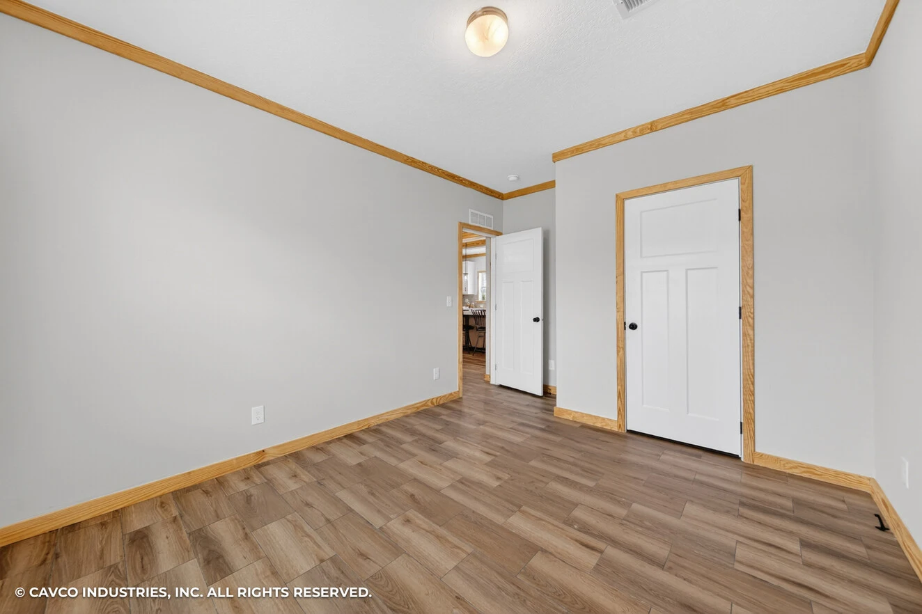 26_c_290_satilla_ly32764d_bed_005_web_copyright_1774469436152_1324_12 Empty room with light gray walls, wood trim, wood-look flooring, two closed white doors, and a ceiling light fixture.