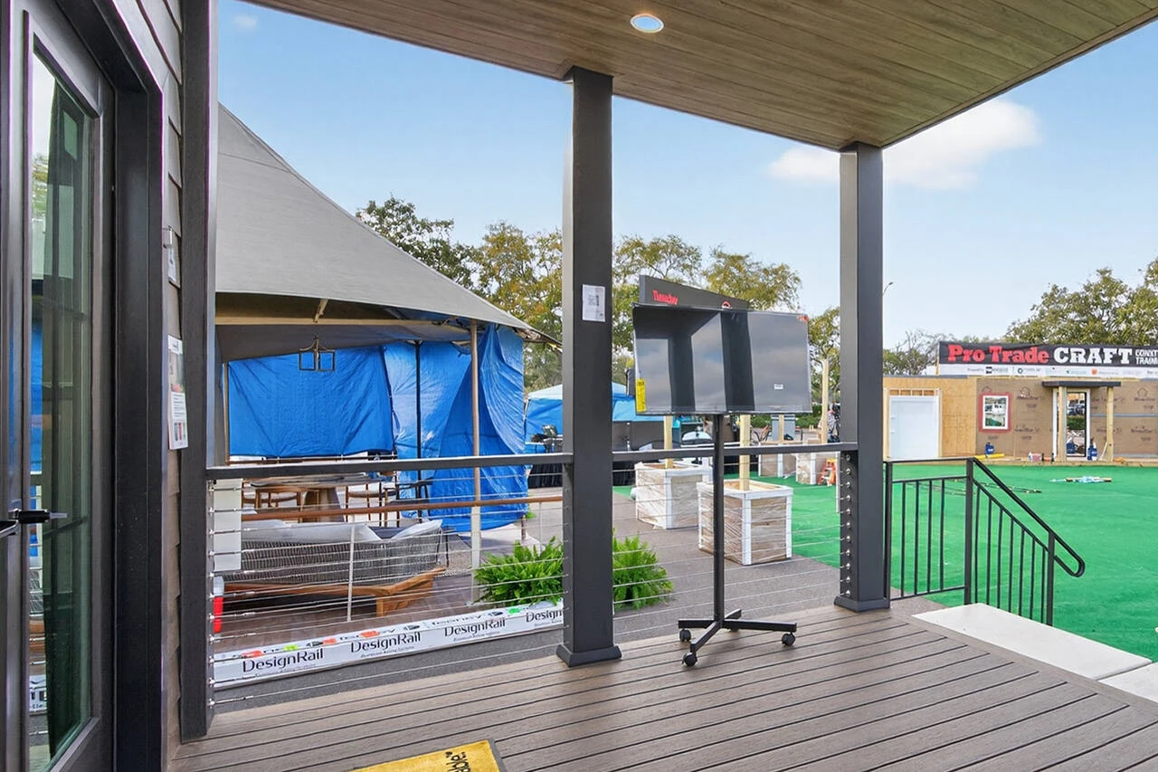 A covered patio with steps leads to an outdoor area featuring a large tent, a rolling TV stand, artificial turf, and a "Pro Trade Craft" sign in the background.