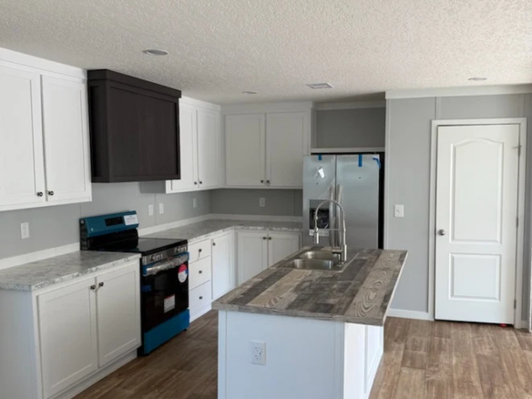 Modern kitchen with white cabinets, a gray island, stainless steel refrigerator, and a blue-covered stove. The floor is wooden, and the walls are light gray with a white door.