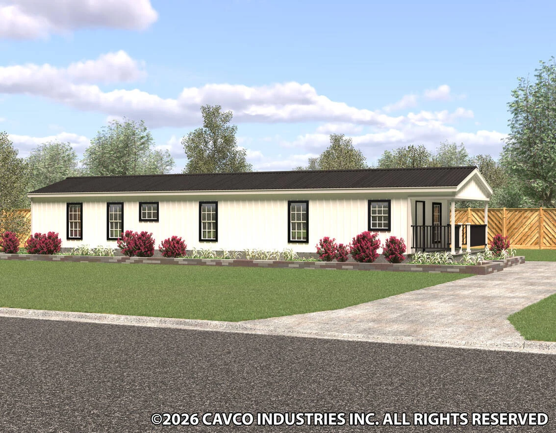 A single-story manufactured home with cream siding, black roof, small front porch, surrounding shrubs, and a paved driveway leading to the entrance.