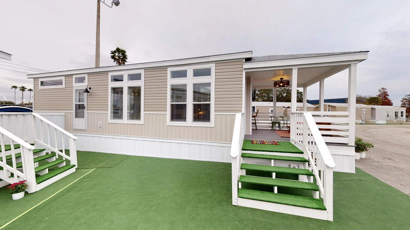 Single-story manufactured home with beige siding, white trim, two sets of stairs, green artificial turf, and a covered porch on the right side.