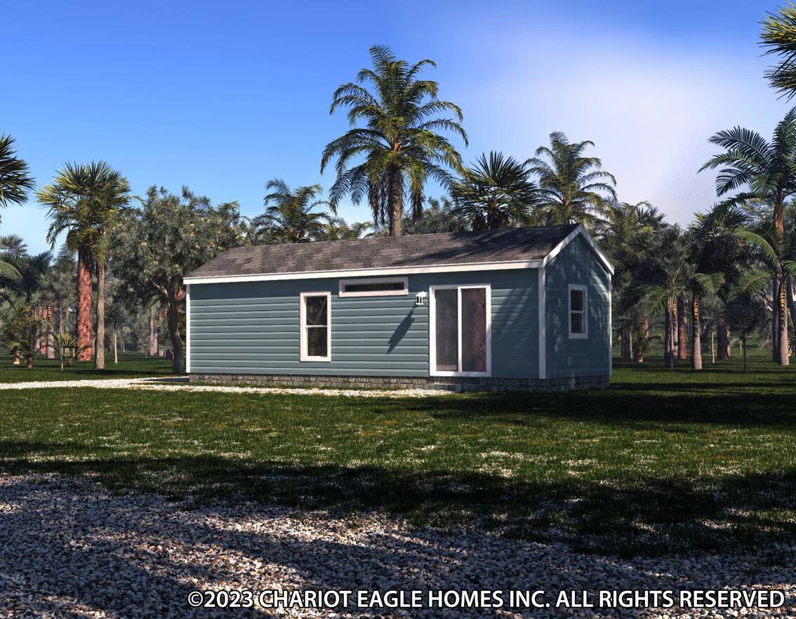 A small, single-story blue manufactured home surrounded by grass, palm trees, and a partly cloudy sky overhead.