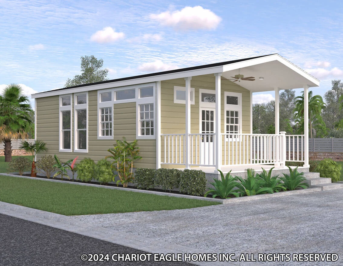 A small, single-story modular home with beige siding, large windows, a covered porch, and surrounding plants under a partly cloudy sky.