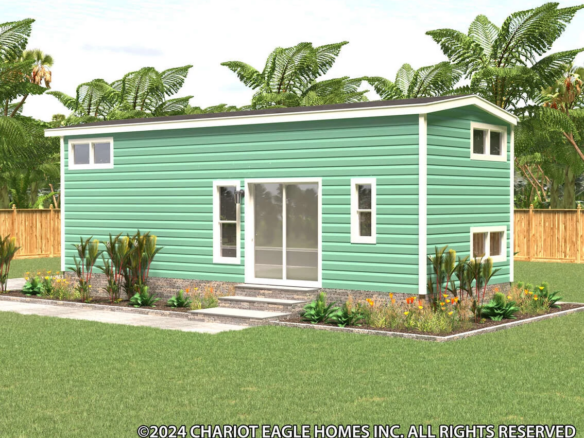 A small green modern tiny house with horizontal siding, large sliding glass doors, and plants in front, set in a fenced yard with tropical trees.