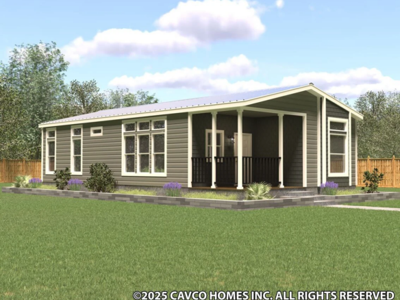 Modern single-story manufactured home with a covered front porch, large windows, and landscaped yard, set against a backdrop of trees and a wooden fence.
