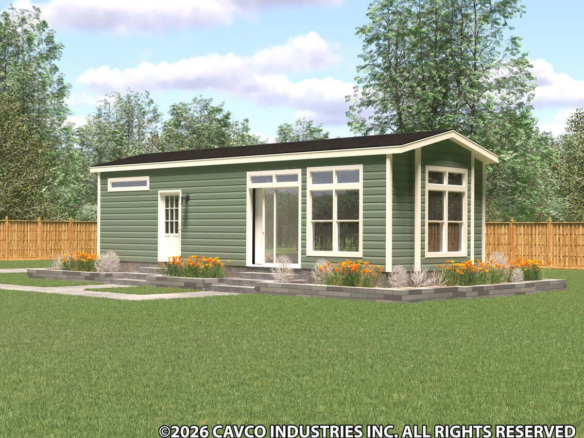 A small green modern modular home with large windows and a black roof, surrounded by a garden and a wooden fence in a grassy yard.