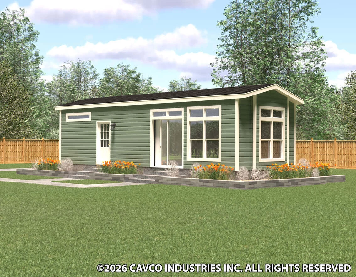A small green modern modular home with large windows and a black roof, surrounded by a garden and a wooden fence in a grassy yard.