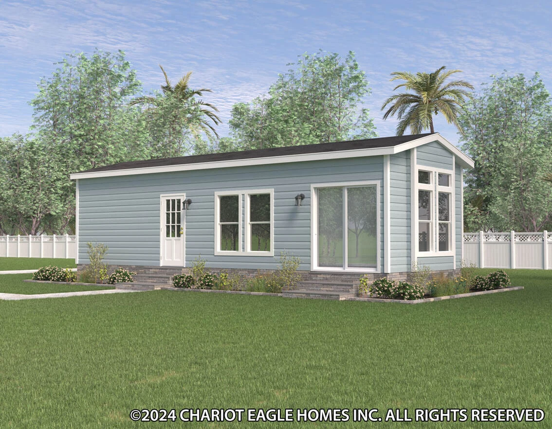 A small, light blue manufactured home with large windows, a white door, and a gabled roof sits on a grassy lawn with landscaping and trees in the background.