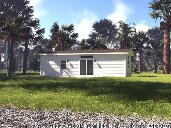A small white modular home with a flat roof sits on a grassy lawn, surrounded by palm trees under a partly cloudy sky.