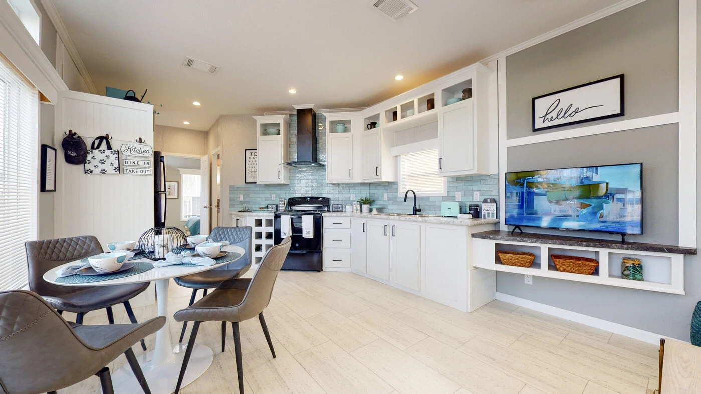 Modern open-concept kitchen and dining area with white cabinets, a round dining table, four chairs, and a wall-mounted TV above shelves with baskets.