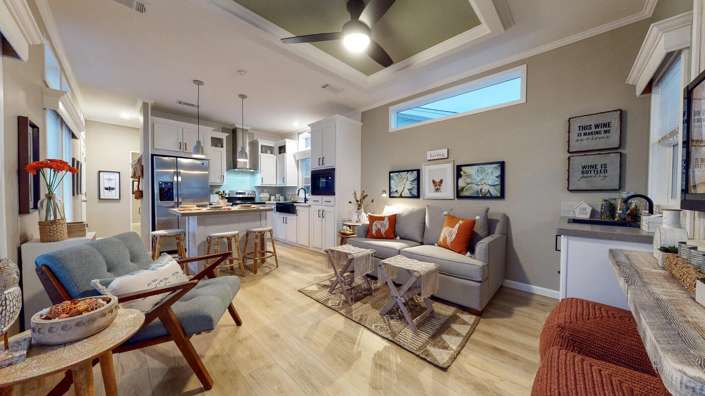 Modern open-concept living room and kitchen with neutral tones, contemporary furniture, and wall art; ceiling fan and recessed lighting provide illumination.