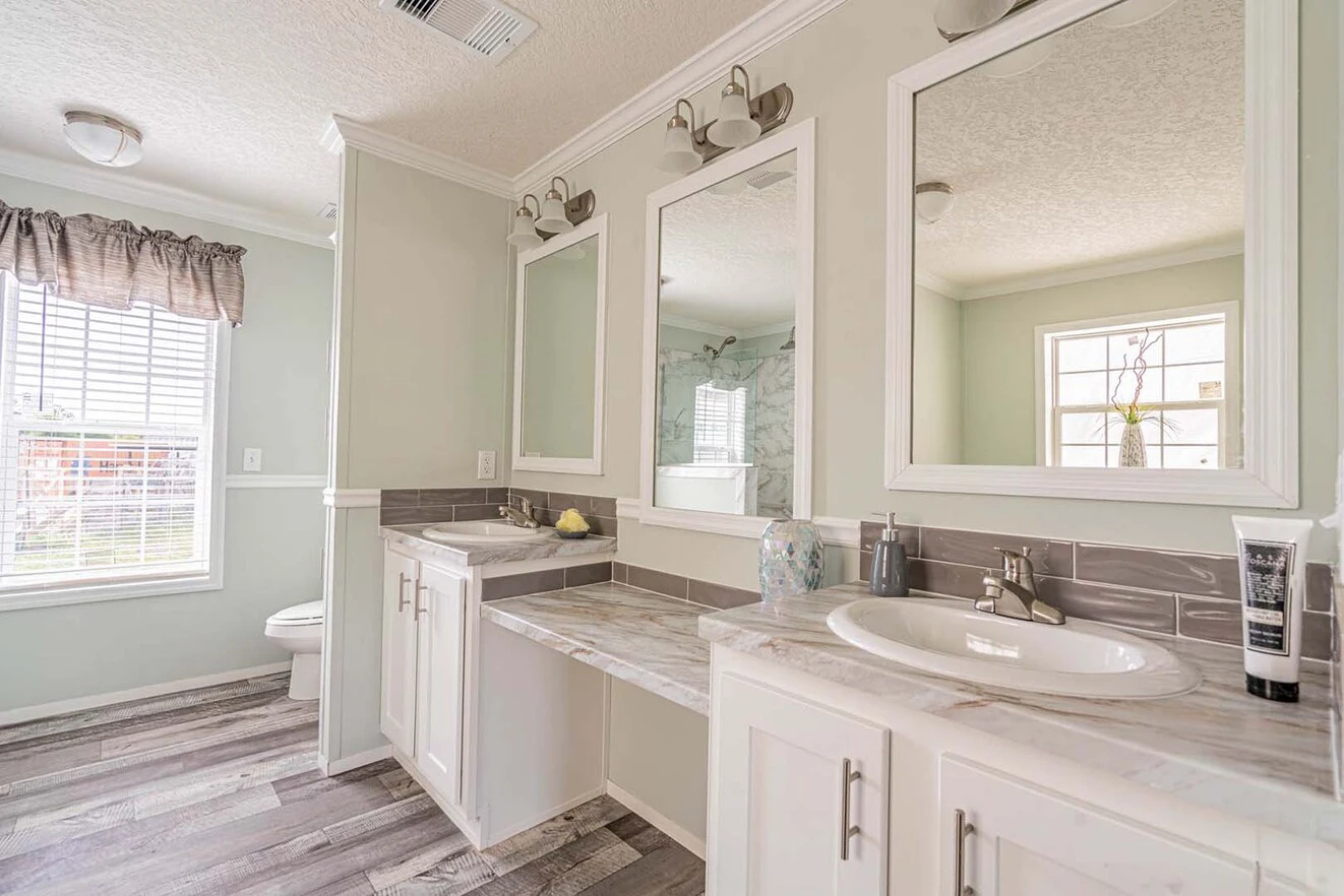 Modern bathroom with two sinks, large mirrors, marble countertops, light wood flooring, and a toilet near a window with blinds.