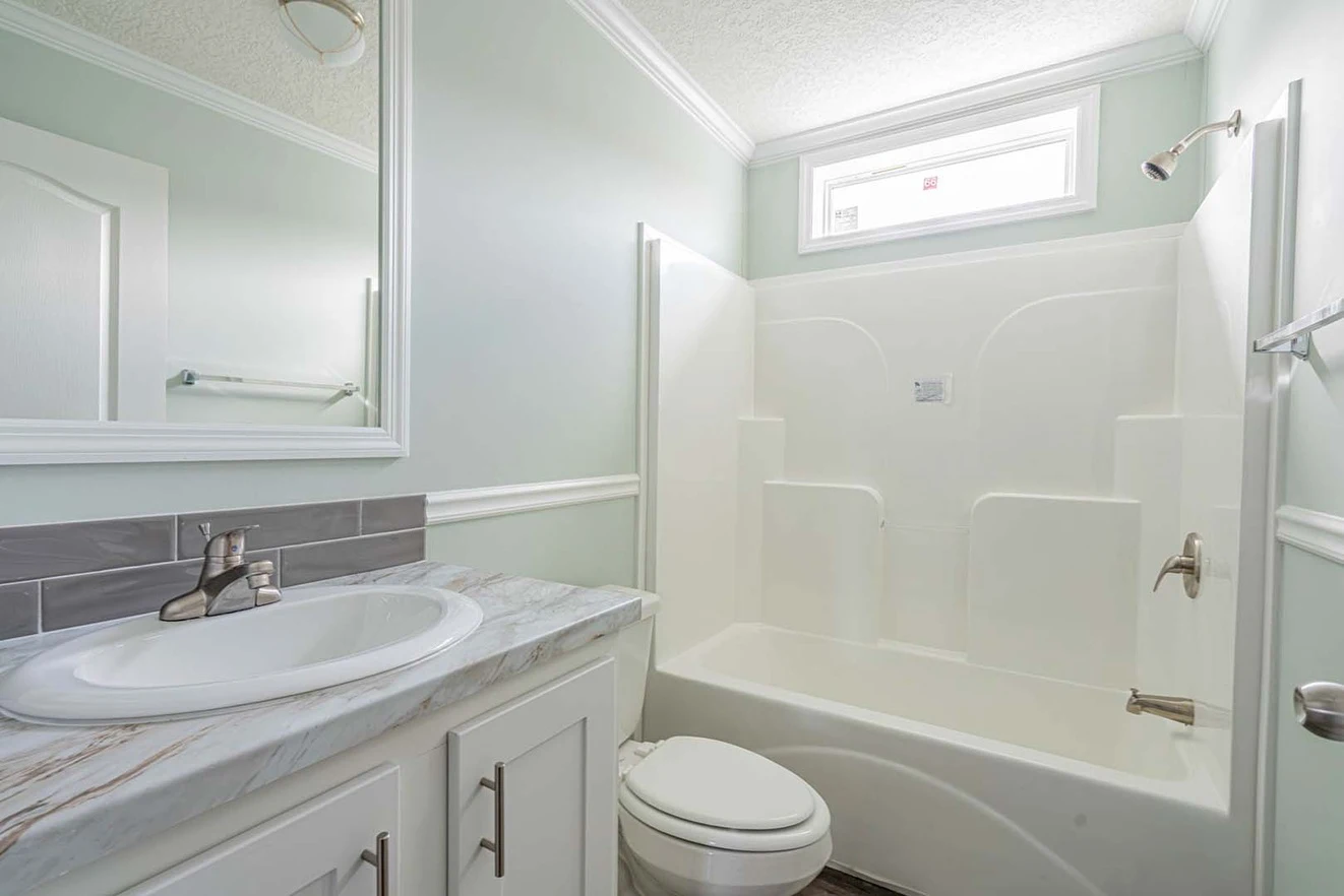 A clean, modern bathroom with a white sink, countertop, toilet, and a bathtub-shower combo under a small window.