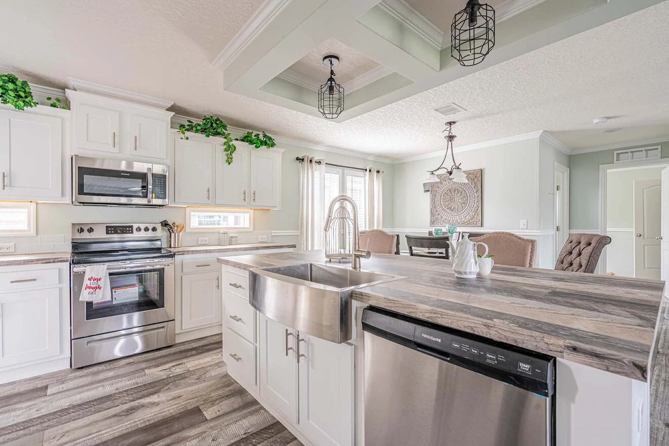 Modern kitchen with white cabinets, stainless steel appliances, a large farmhouse sink, wood-patterned countertops, and decorative pendant lights over the island.