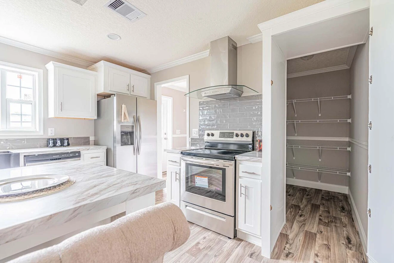 Modern kitchen with stainless steel appliances, white cabinets, marble countertops, and an adjacent open pantry with empty shelves.