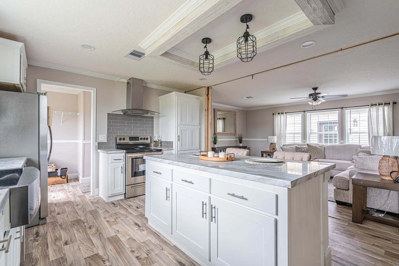 Bright, modern kitchen with white cabinets, marble countertops, stainless steel appliances, and an island, adjoining an open living room with light wood flooring.