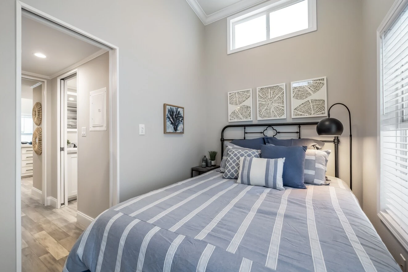 chariot_eagle_eagle_eg12341a_bedroom_0729_1_1673903455435_1323_12 A neatly made bed with striped bedding sits in a small, bright bedroom with light walls, modern decor, and a window above the headboard.