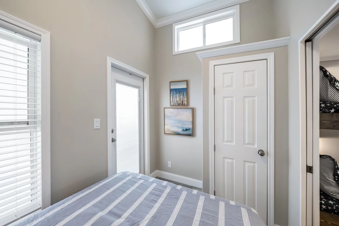 chariot_eagle_eagle_eg12341a_bedroom_0813_1_1673903449880_1323_12 Small bedroom with a bed, striped bedding, a closed closet door, a window above, a glass door, wall art, and light-colored walls.