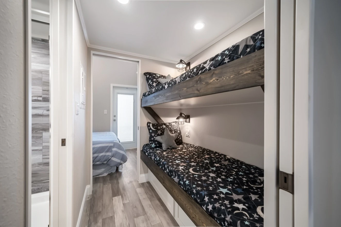 chariot_eagle_eagle_eg12341a_bunks_0581_1_1673903442289_1323_12 Narrow hallway with built-in wooden bunk beds featuring star and moon bedding; a bedroom with a striped bedspread is visible at the end of the hall.
