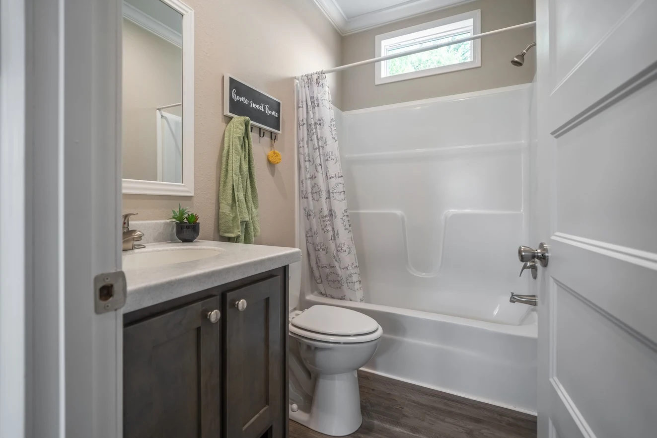 A small bathroom with a white bathtub and shower, closed toilet, dark vanity with sink, wall mirror, towel, and a window above the tub.